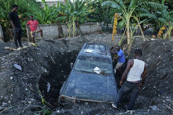 2025 оны 11-р сарын 6-ны Пүрэв гарагт Гаити улсын Петит-Гоав хотод Мелисса хар салхины дараа хэсэгчлэн булсан тээврийн хэрэгслийг зайлуулахаар оршин суугчид ажиллаж байна. (Зураг: AP Photo/Odelyn Joseph) - Sputnik Монгол Улс