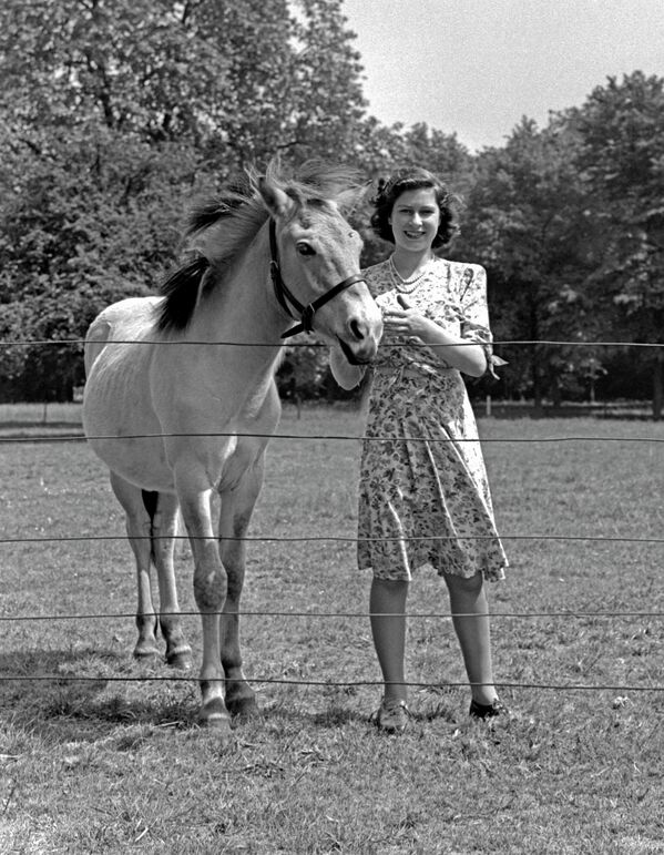 Их Британи, Беркшир — 1944 оны 5-р сарын 30-нд Виндзорын цайзын цэцэрлэгт морьтой зогсож буй гүнж Элизабет (хожмоо Хатан хаан Элизабет II). (Зураг: Лиза Шеридан/Studio Lisa/Hulton Archive/Getty Images) - Sputnik Монгол Улс