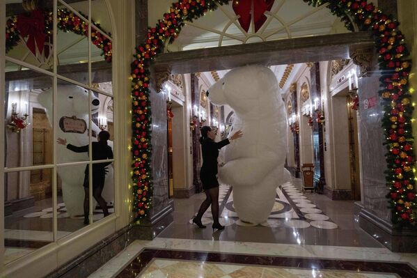 2025 оны 12-р сарын 24-ний Лхагва гарагт Бээжинд Зул сарын баярын өмнөх өдөр зочдыг хүлээн авсны дараа зочид буудлын ажилтан цагаан баавгайн сахиусанд тусалж байна. (AP Photo/Ng Han Guan) - Sputnik Монгол Улс