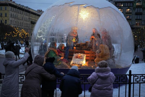 2025 оны 12-р сарын 24-ний Лхагва гарагт Оросын Санкт-Петербург хотод Зул сарын баярын өмнө Казань сүмийн ойролцоо байрлуулсан Зул сарын хүүхдийн орыг харж буй хүмүүс. (AP Photo/Dmitri Lovetsky) - Sputnik Монгол Улс